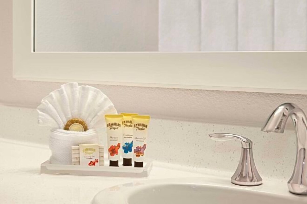 A bathroom sink with a white vanity, a mirror, and three toiletry bottles labeled 'Hawaiian Tropic'.