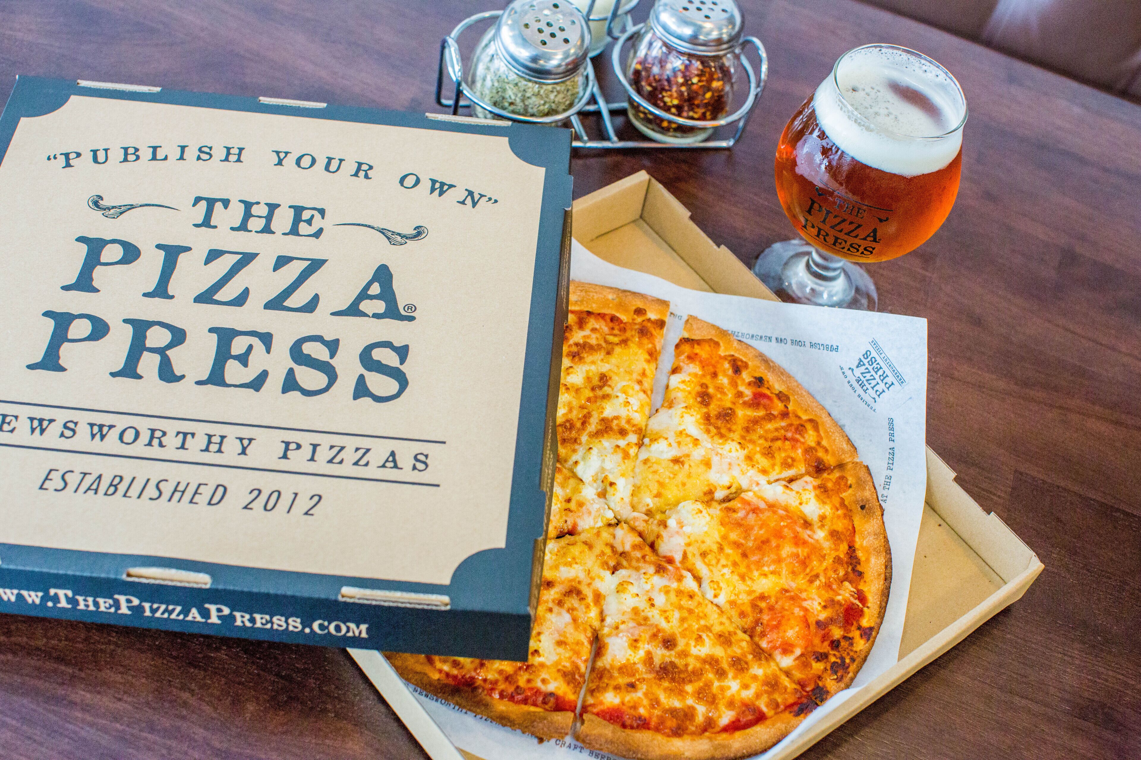 A pizza box with a pizza slice and a glass of beer on a wooden table.