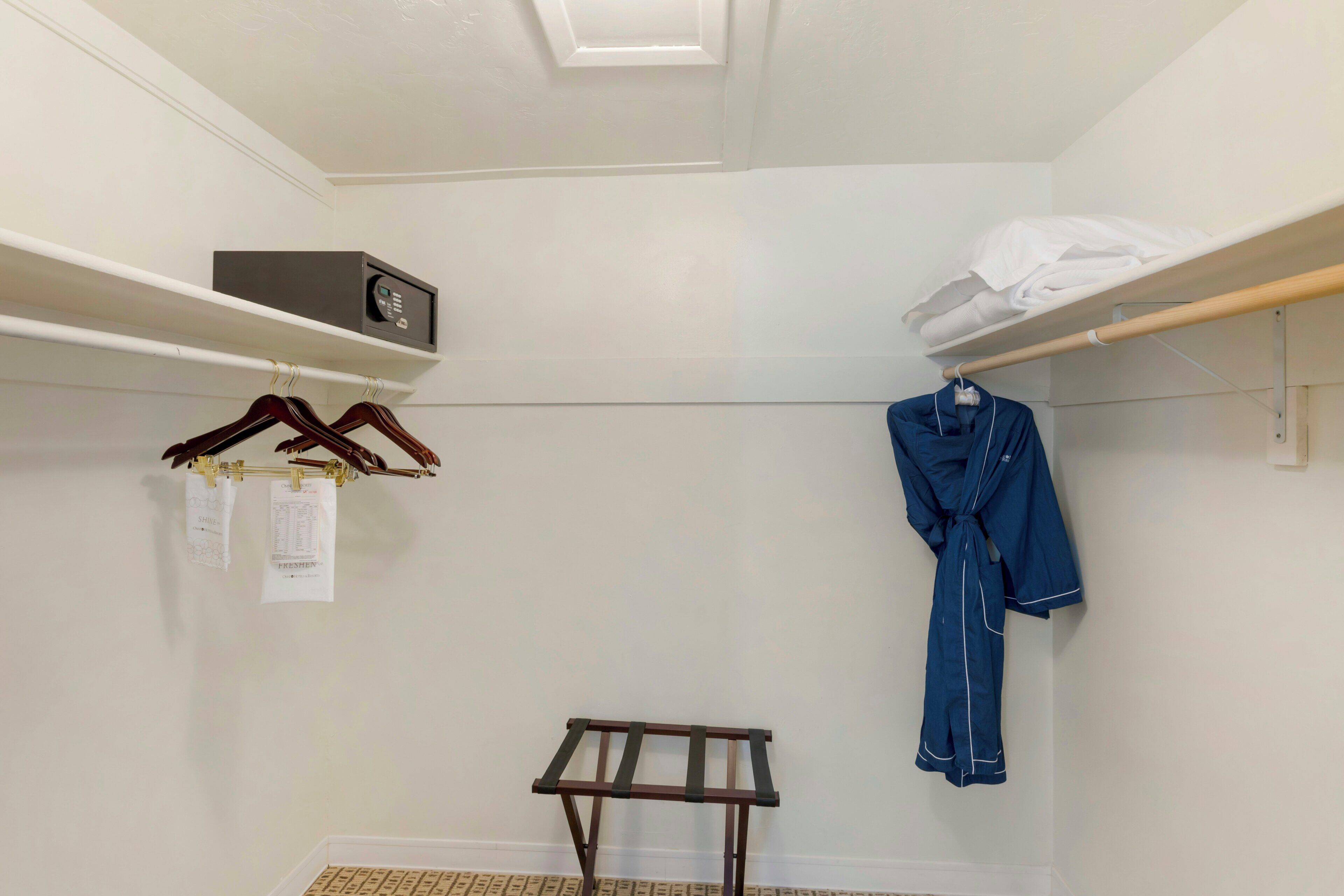 Ein kleiner, gut beleuchteter Raum mit Decke in Weiß, einem Holzgestell mit Kleiderbügeln, einem Wäscheständer und einem weißen Handtuch auf einer Ablagefläche.