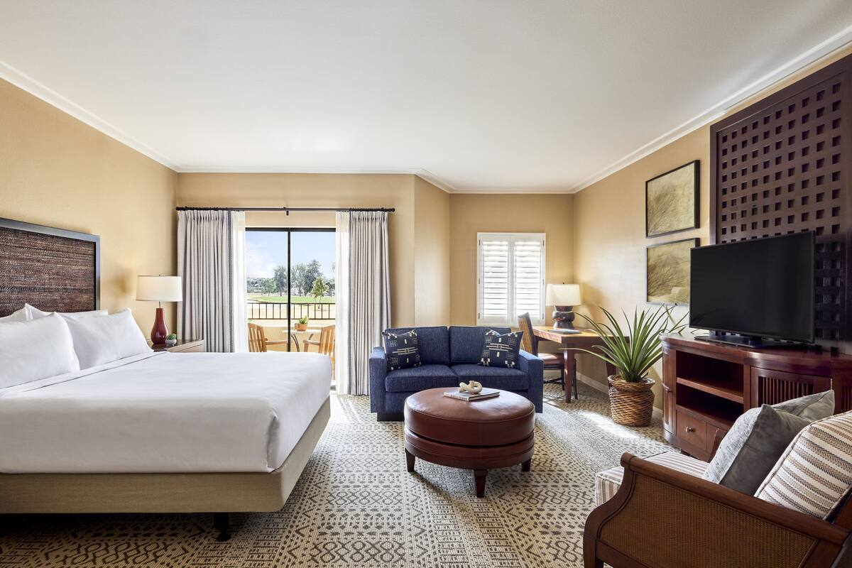Une chambre d’hôtel avec un grand lit, un canapé, une table basse, une télévision et un balcon avec vue.