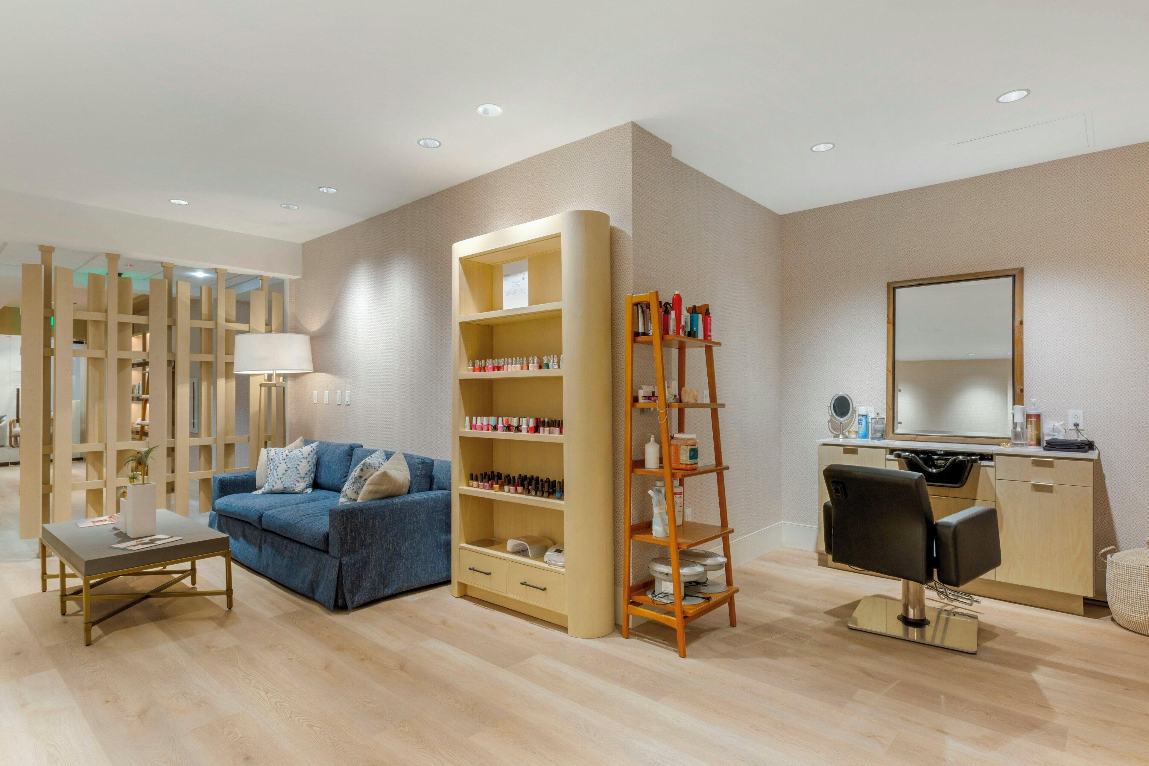 A modern living room with a blue sofa, a wooden bookshelf, a desk, and a mirror.