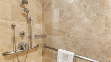 Un espace douche équipé d’un pommeau de douche à main, d’un pommeau de douche fixé au mur et d’une barre d’appui.