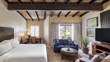 Quarto de hotel com uma cama grande, um sofá, uma televisão e uma área de refeições com mesa e cadeiras.