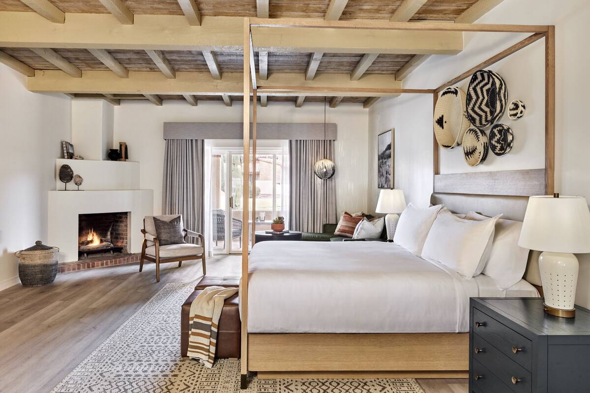 Une chambre spacieuse dotée d’un grand lit, d’une cheminée, d’un plafond en bois et offrant une vue sur l’extérieur.