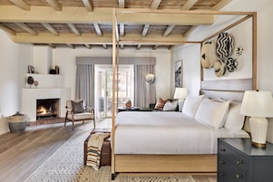 A spacious bedroom with a large bed, a fireplace, a wooden ceiling, and a view of the outdoors.