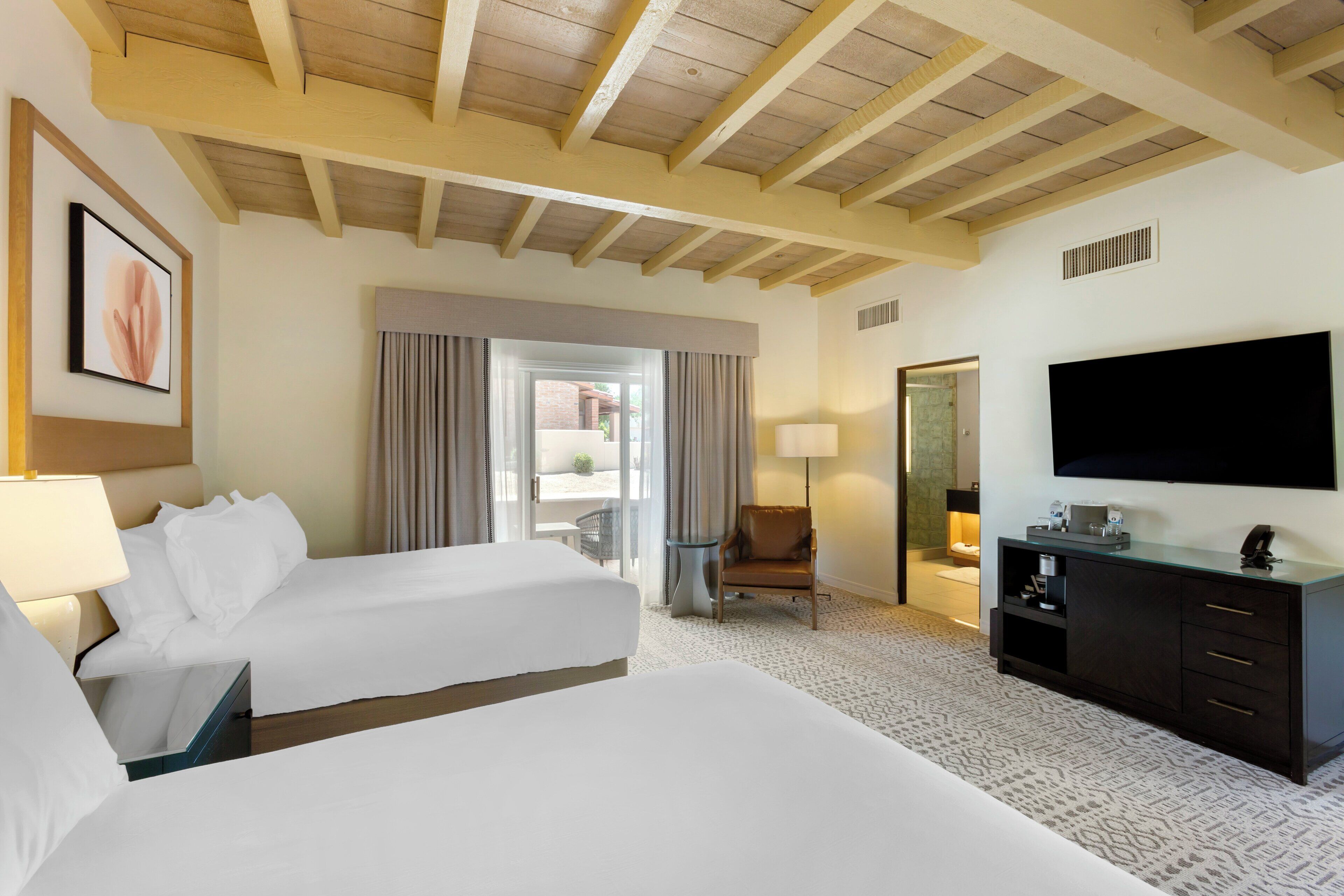 Habitació d'hotel amb dos llits, un televisor de pantalla plana, un escriptori i una cadira.