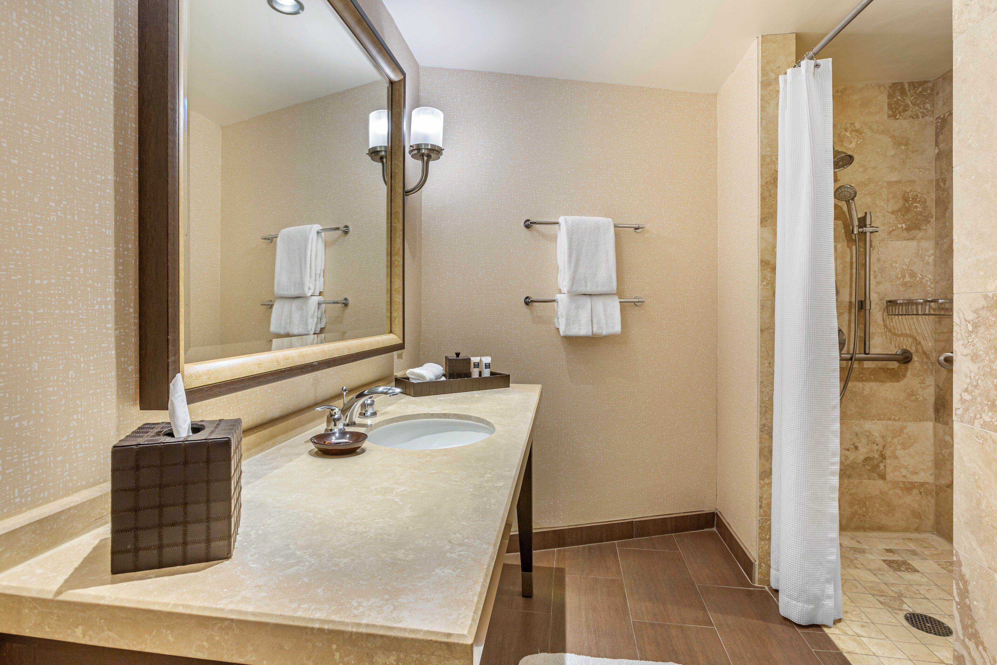A bathroom with a sink, mirror, towel rack, and shower.
