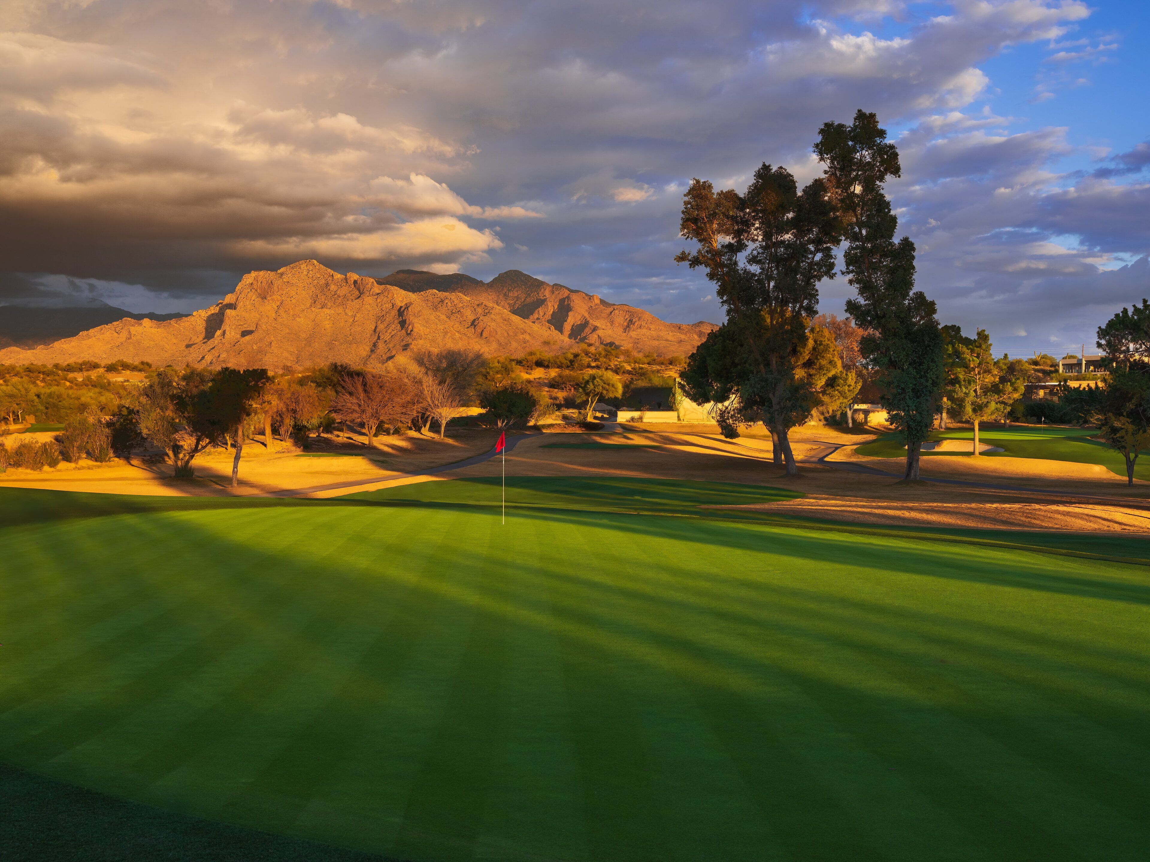 A golf course with a flag, trees, and mountains in the background.