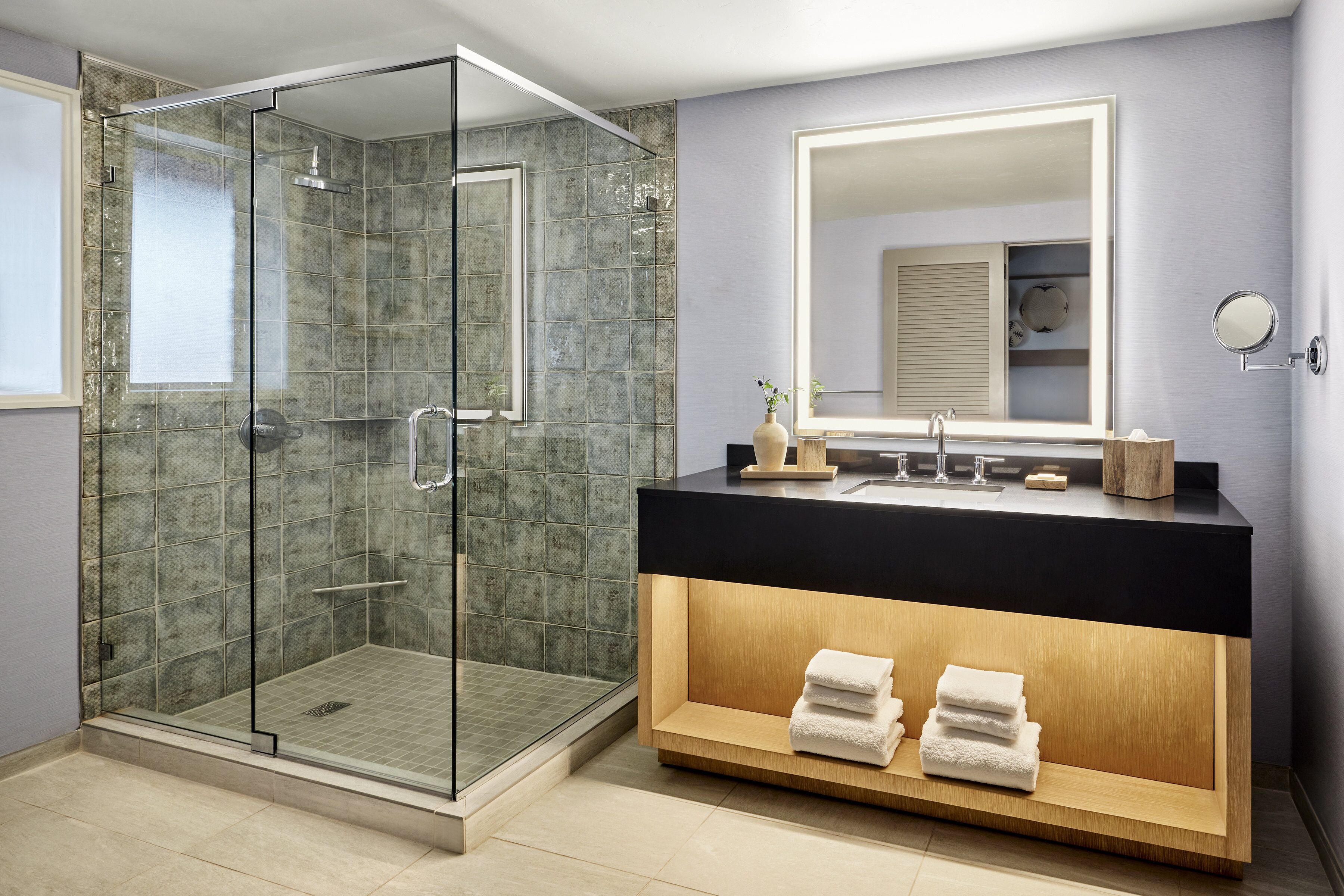 Une salle de bain moderne avec une douche à parois de verre, un meuble-lavabo doté d’un plan de travail noir et un miroir au-dessus.