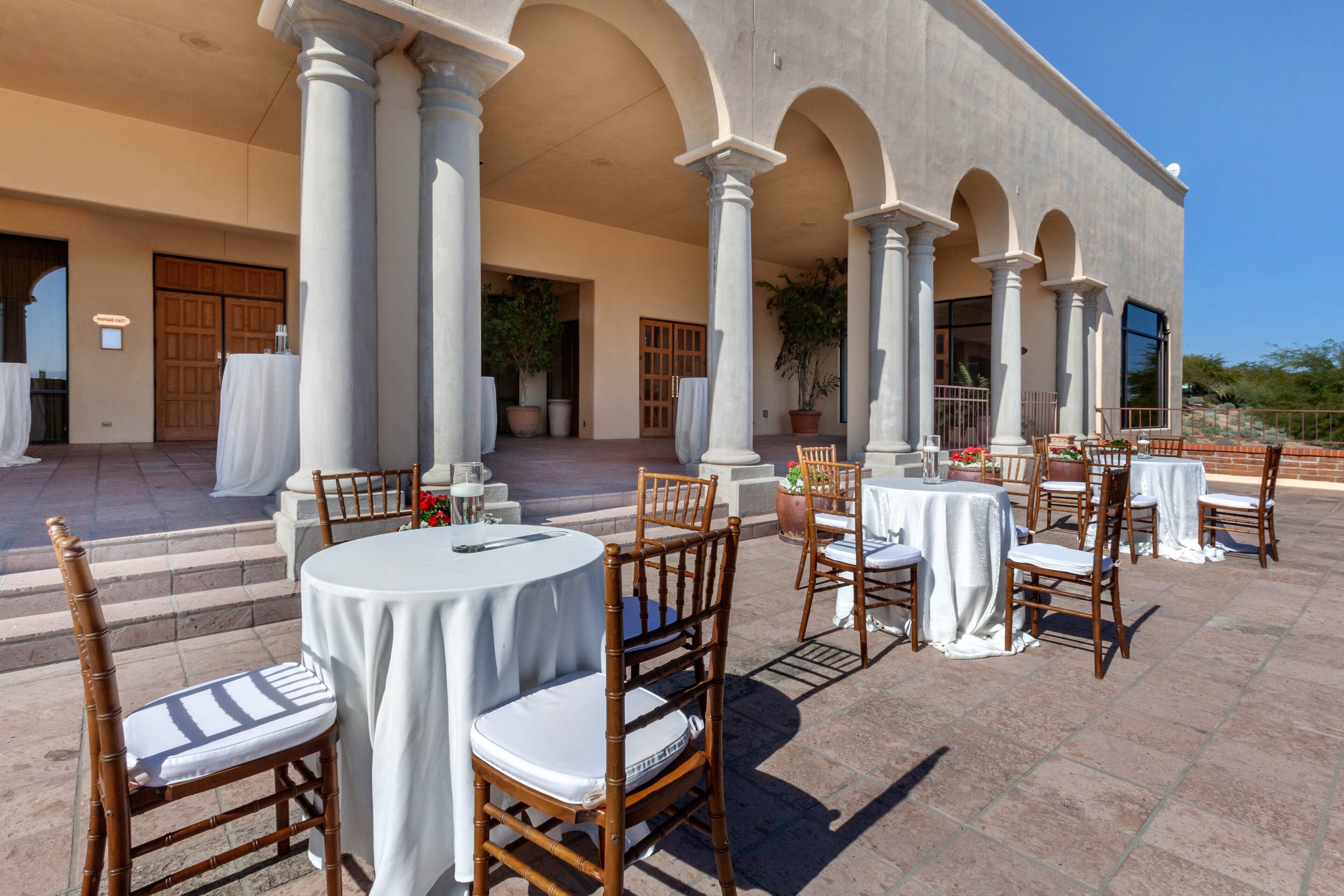 An outdoor patio with round tables and chairs, columns, and potted plants.