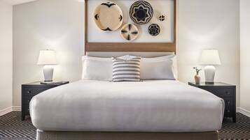 A neatly made bed with white linens, two bedside tables with lamps, and a wall-mounted art display above the bed.