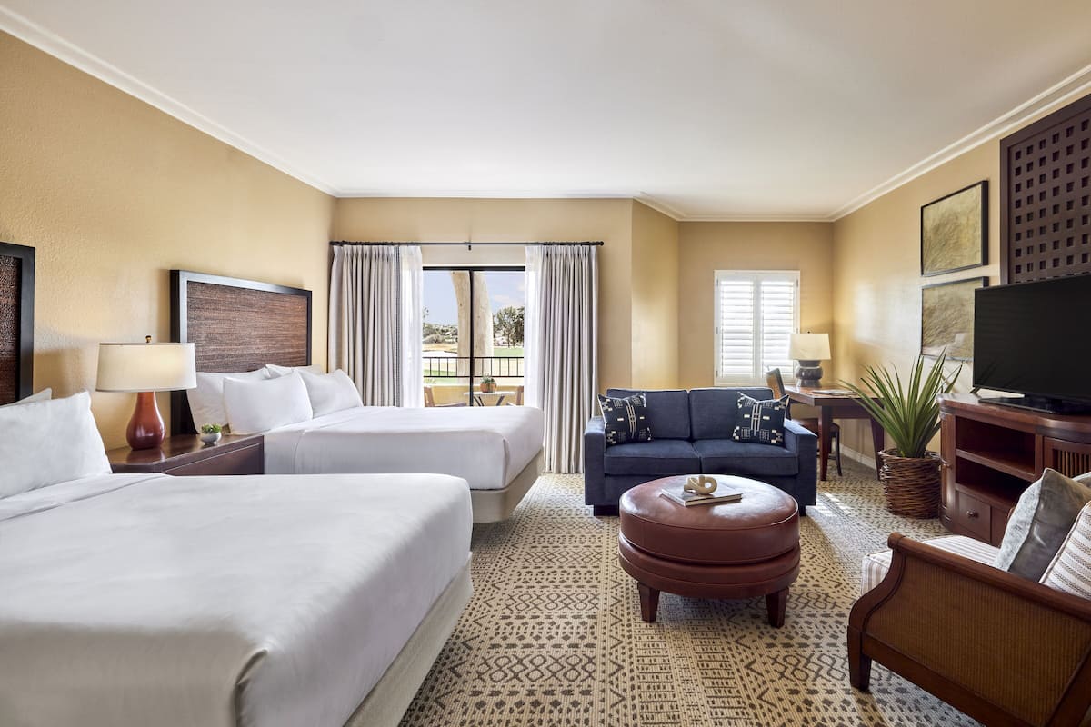 Une chambre d’hôtel avec deux lits, un canapé, une télévision et un coin repas comprenant une table et des chaises.