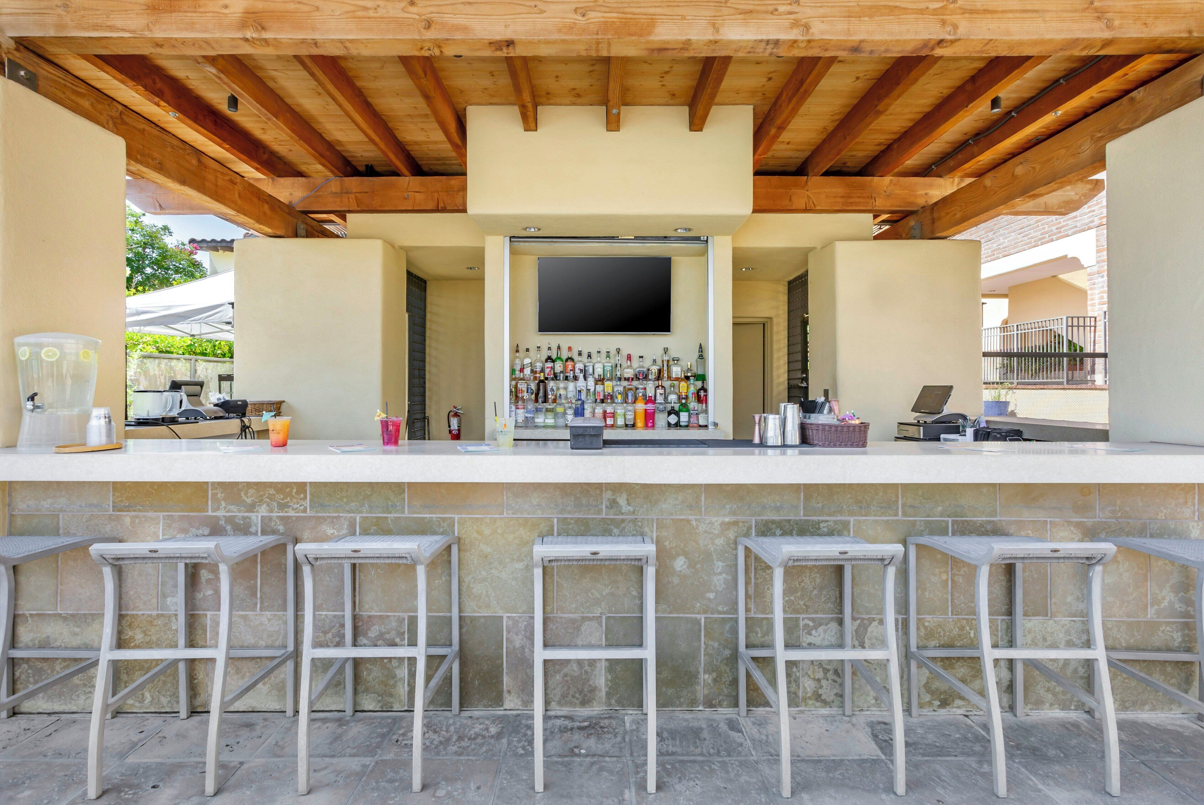 An outdoor bar area with a flat-screen TV, a variety of bottles, and bar stools.