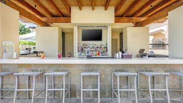 An outdoor bar area with a flat-screen TV, a variety of bottles, and bar stools.
