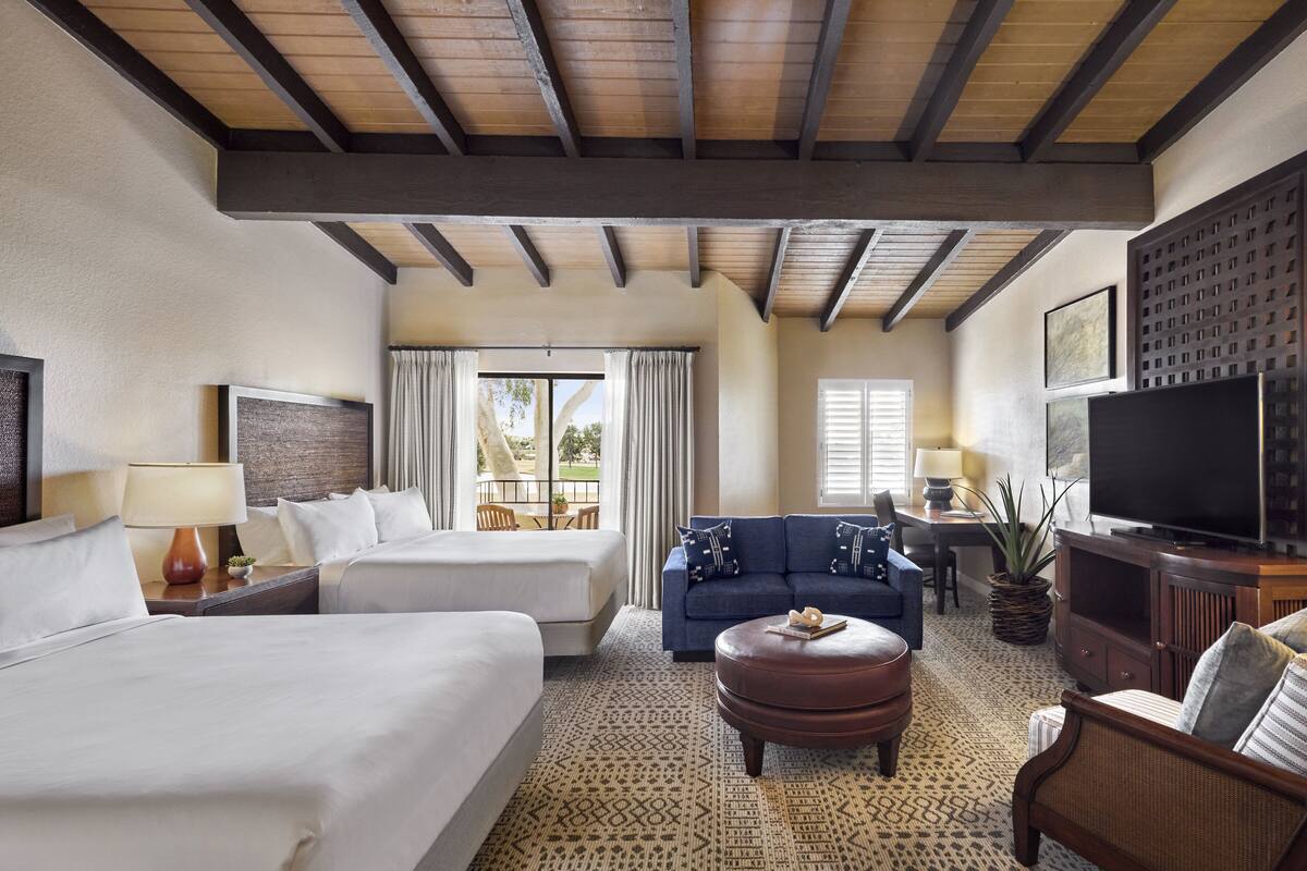 Une chambre d’hôtel avec deux lits, un canapé, une télévision et un coin repas comprenant une table et des chaises.