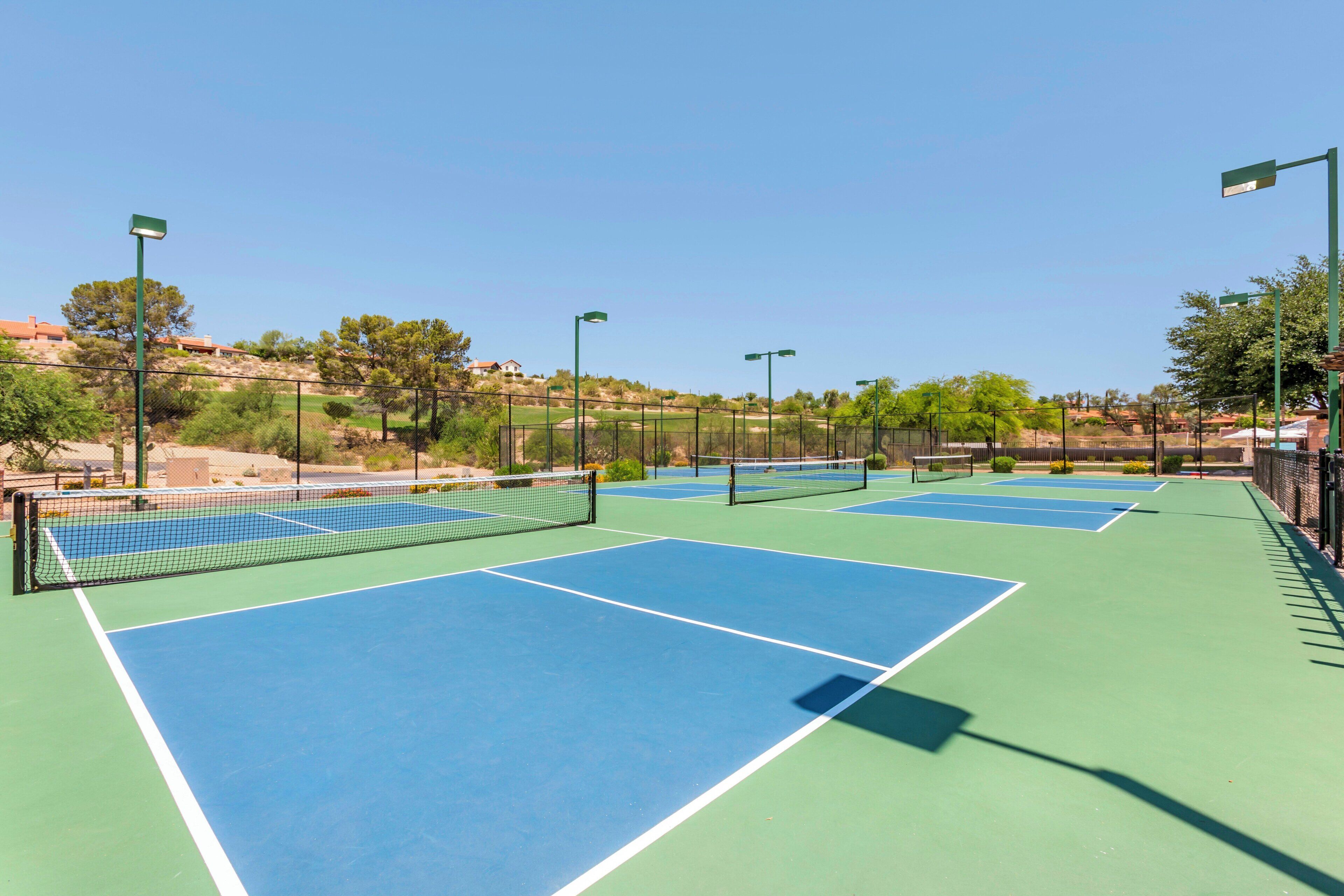 A tennis court with multiple courts, surrounded by a fence, and street lamps.