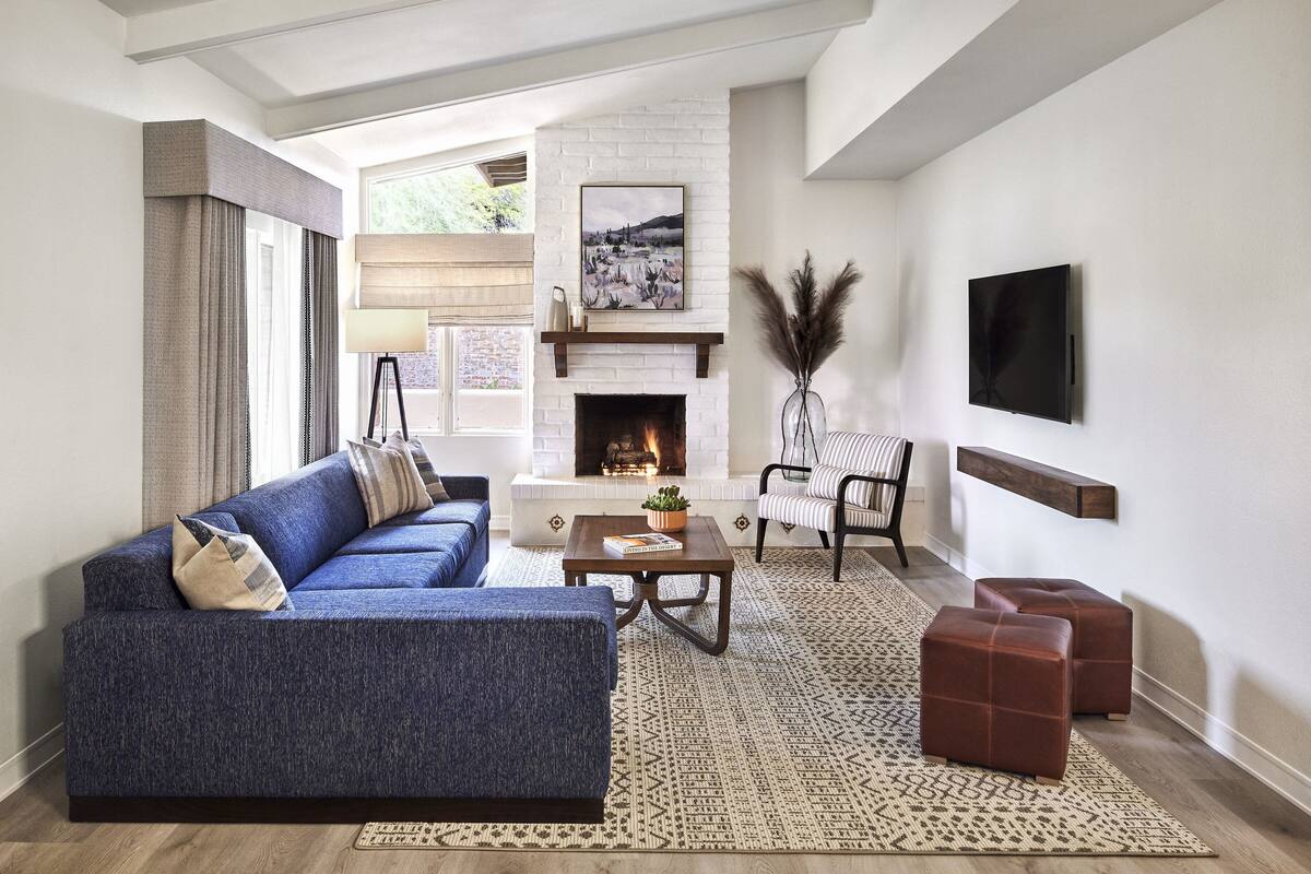 Un salon moderne avec un canapé bleu, une cheminée, un téléviseur fixé au mur et un tapis à motifs.