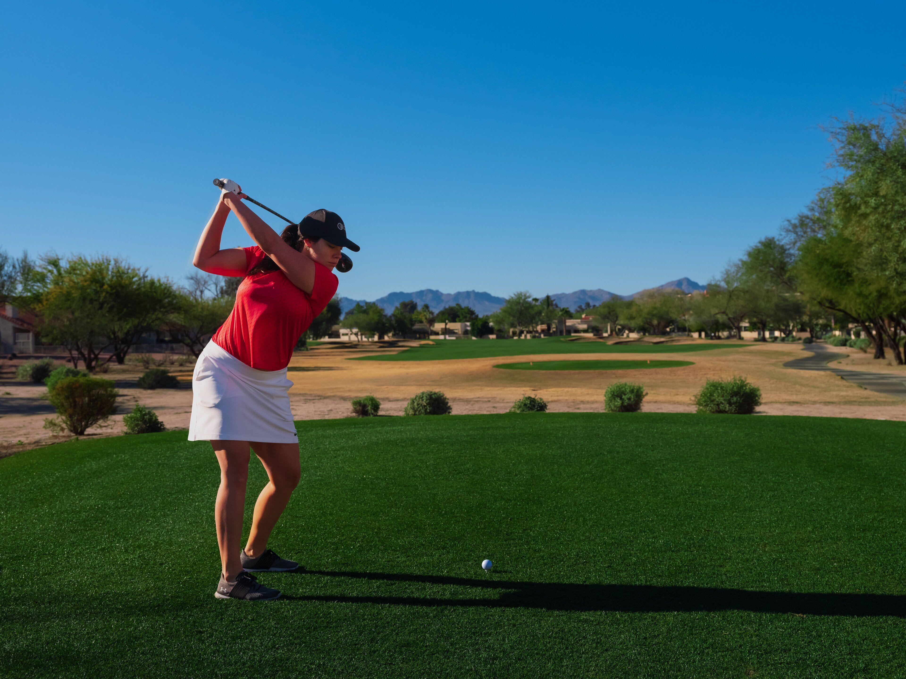 A golf course with a clear sky, trees, and distant mountains.