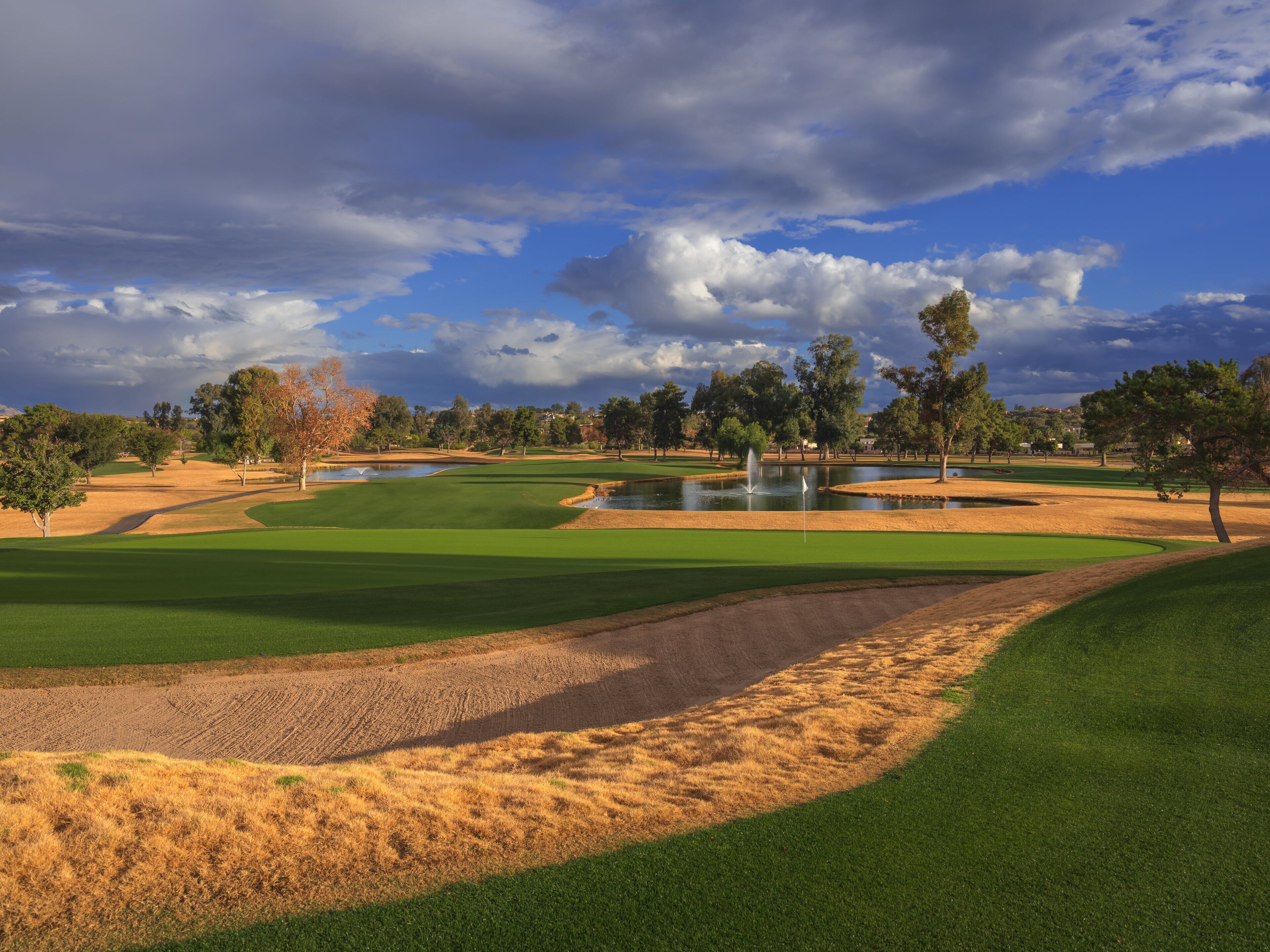 Un campo de golf con un estanque, búnkeres de arena y árboles.