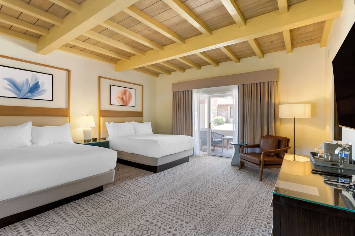 Une chambre d’hôtel avec deux lits, un bureau avec une lampe, une chaise et une vue sur l’extérieur grâce à une porte coulissante.