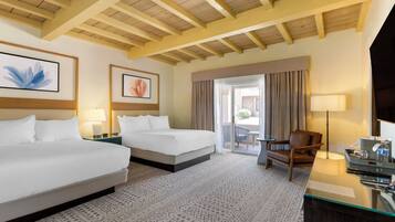 A hotel room with two beds, a desk with a lamp, a chair, and a view of the outdoors through a sliding door.