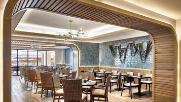 A restaurant with wooden flooring, wicker chairs, and a modern chandelier.