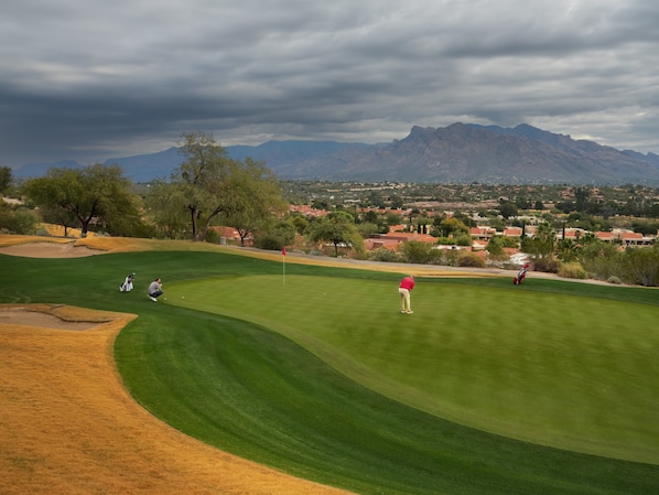 Un parcours de golf offrant une vue sur une ville et, au loin, sur des montagnes.