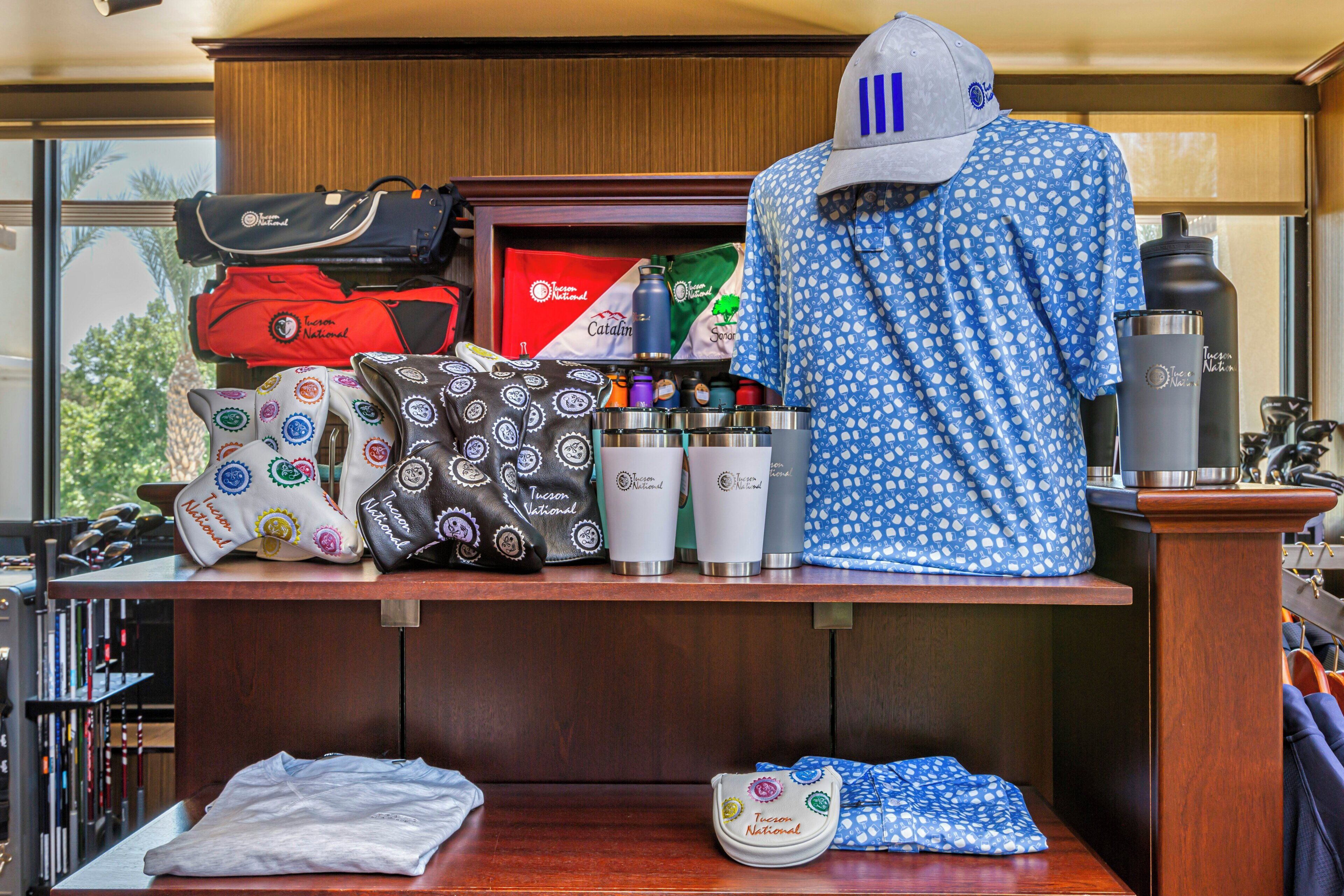 Exhibición de artículos de viaje que incluyen bolsos, una gorra y botellas de agua con el logotipo 'Tucson National'.