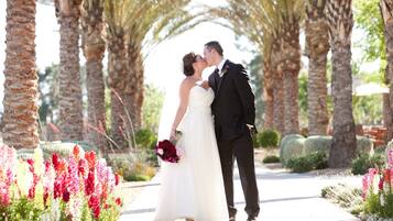 A couple kissing under a palm tree archway in a garden setting.