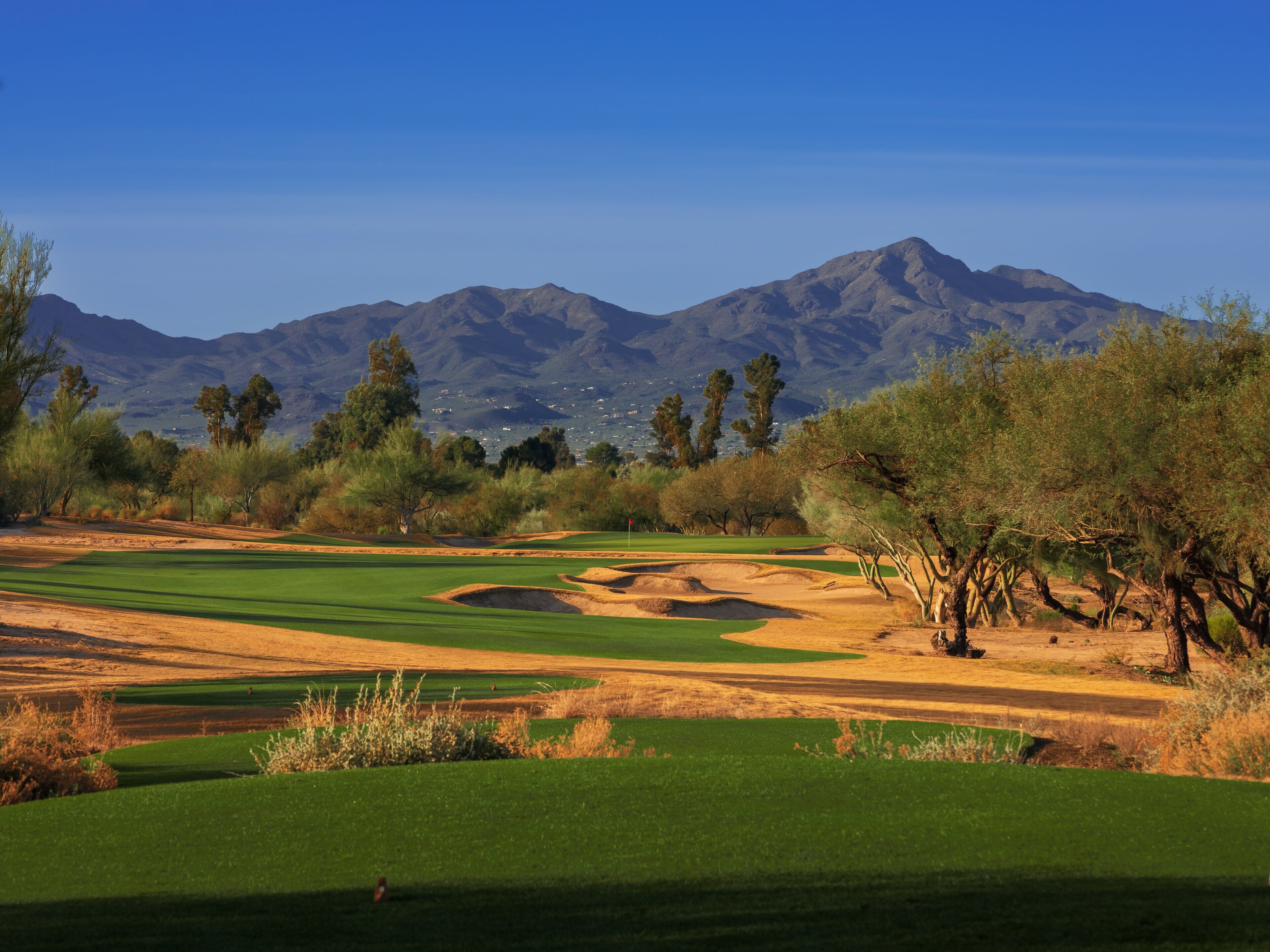 Camp de golf amb muntanyes al fons, búnquers de sorra i vegetació escassa.