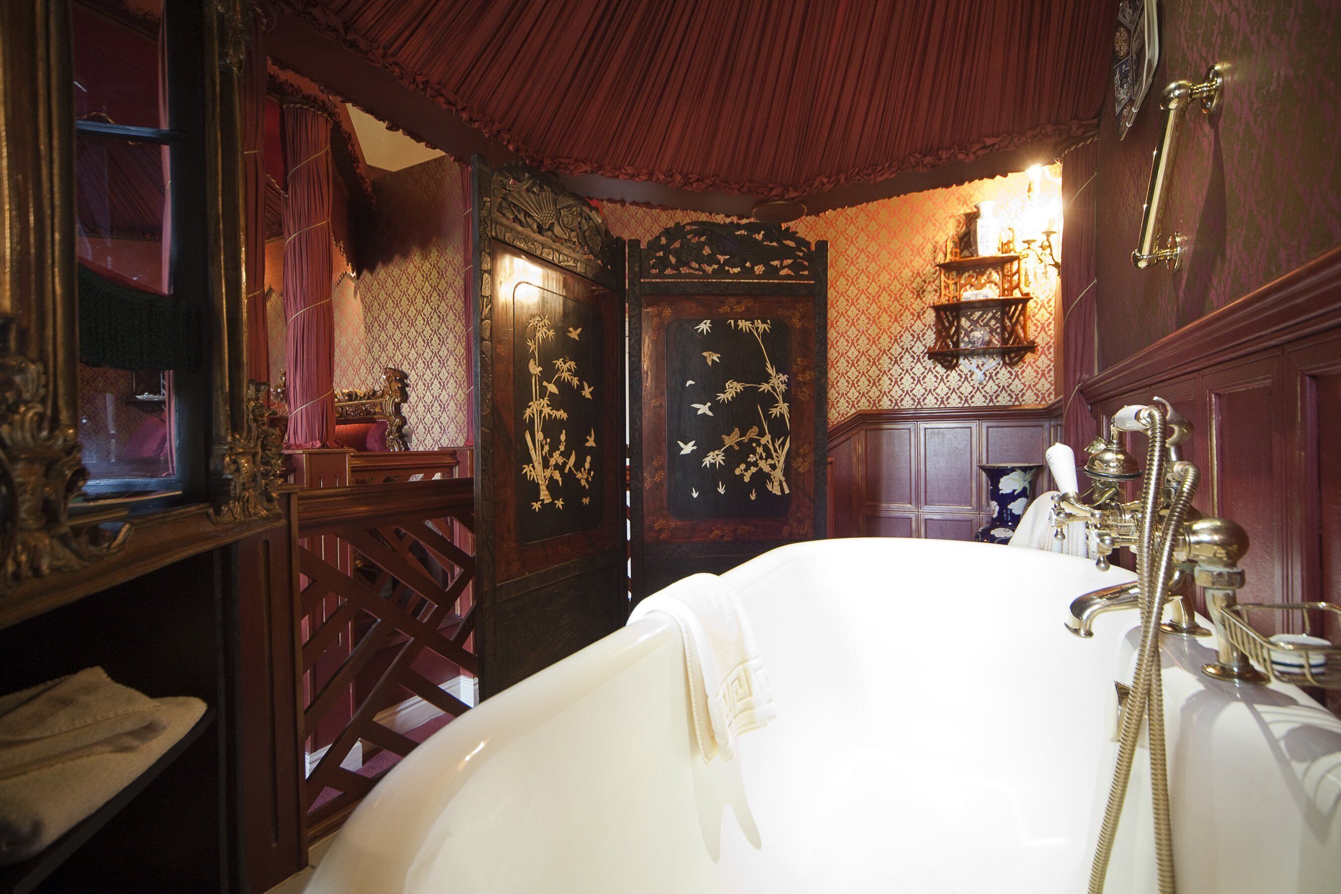 Un baño clásico con una bañera independiente, puertas de madera decoradas y un espejo de estilo vintage.