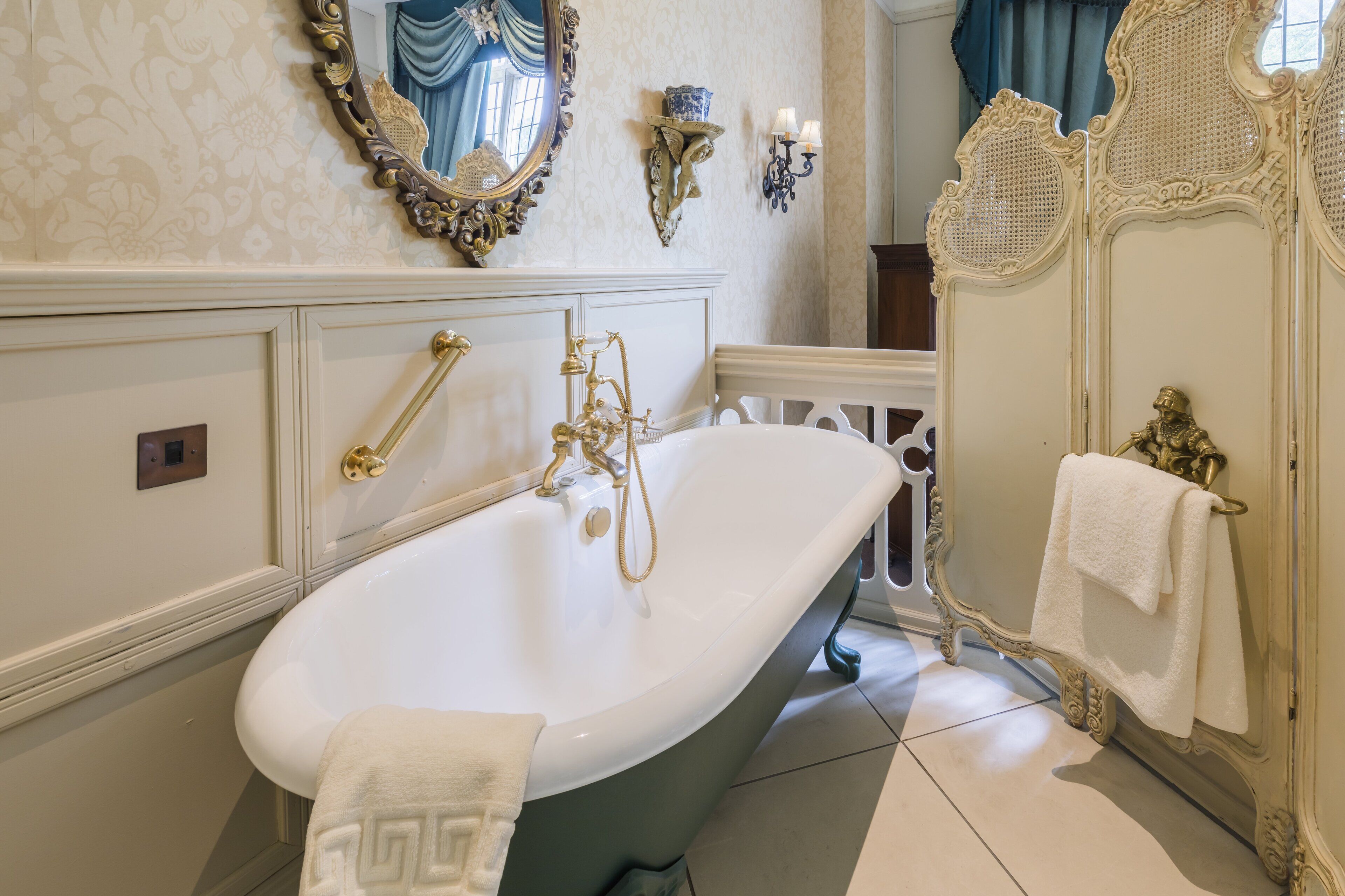 A classic bathroom with an ornate bathtub, a large mirror, and a decorative wall panel.
