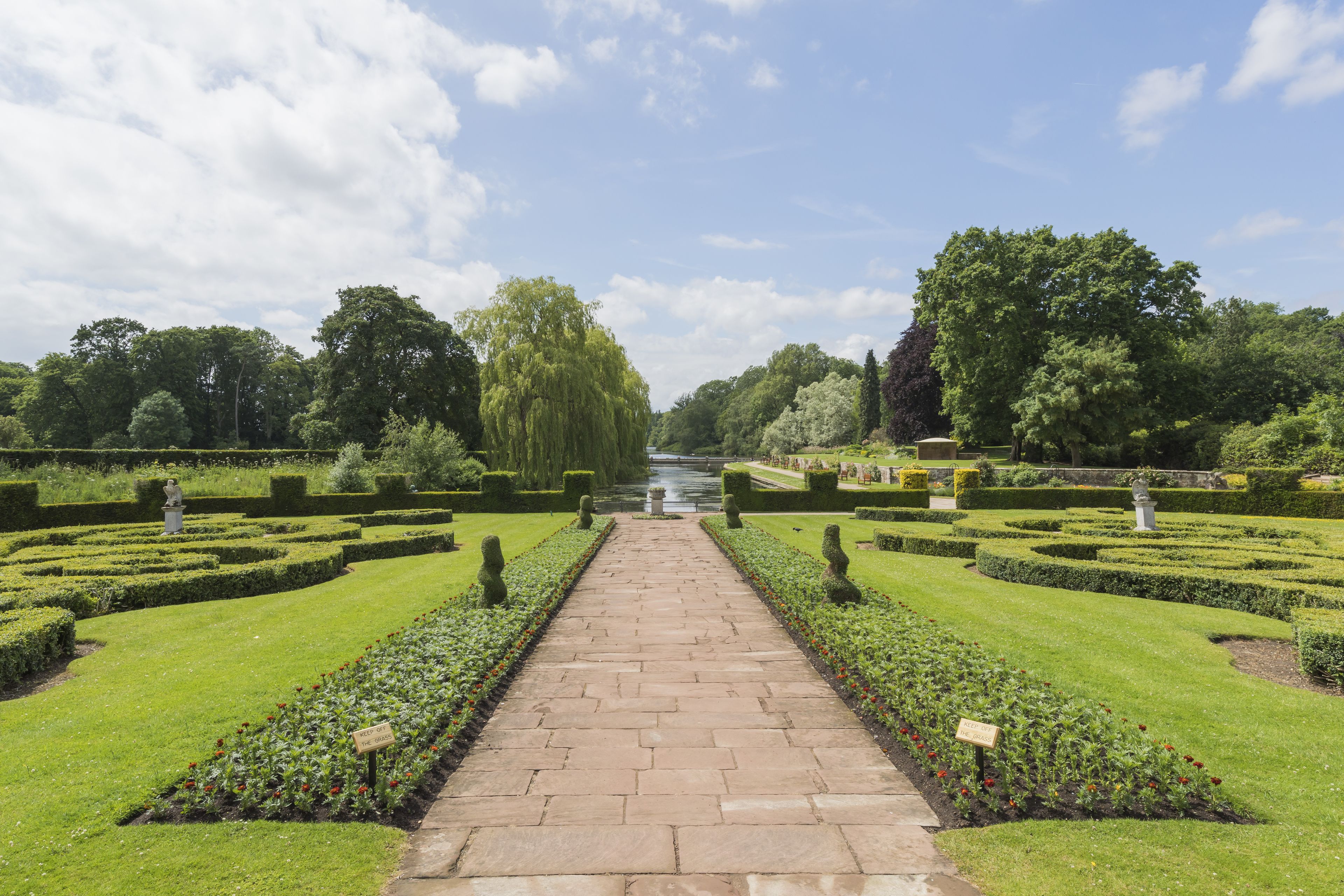 A formal garden with a central pathway, manicured lawns, and neatly trimmed hedges.