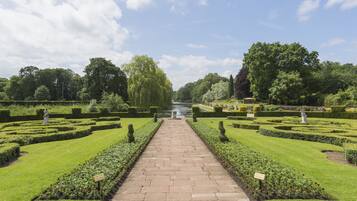 A formal garden with a central pathway, manicured lawns, and neatly trimmed hedges.