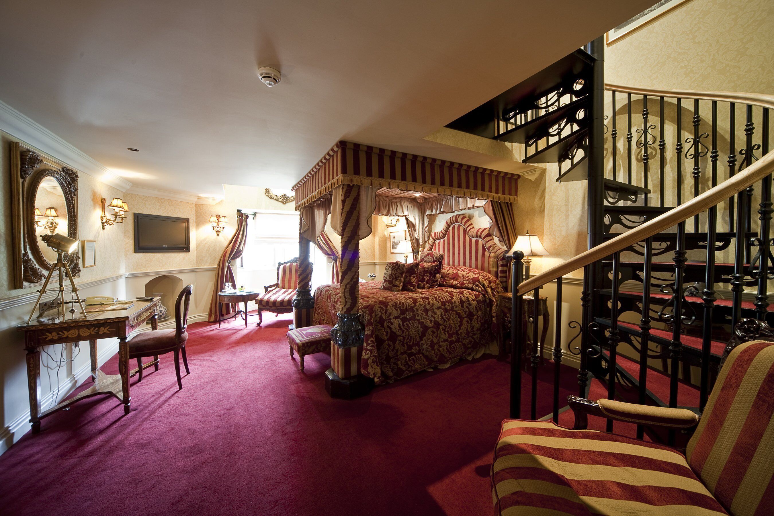 Une chambre à coucher avec un lit à baldaquin, un bureau avec une chaise, un escalier et un grand miroir.