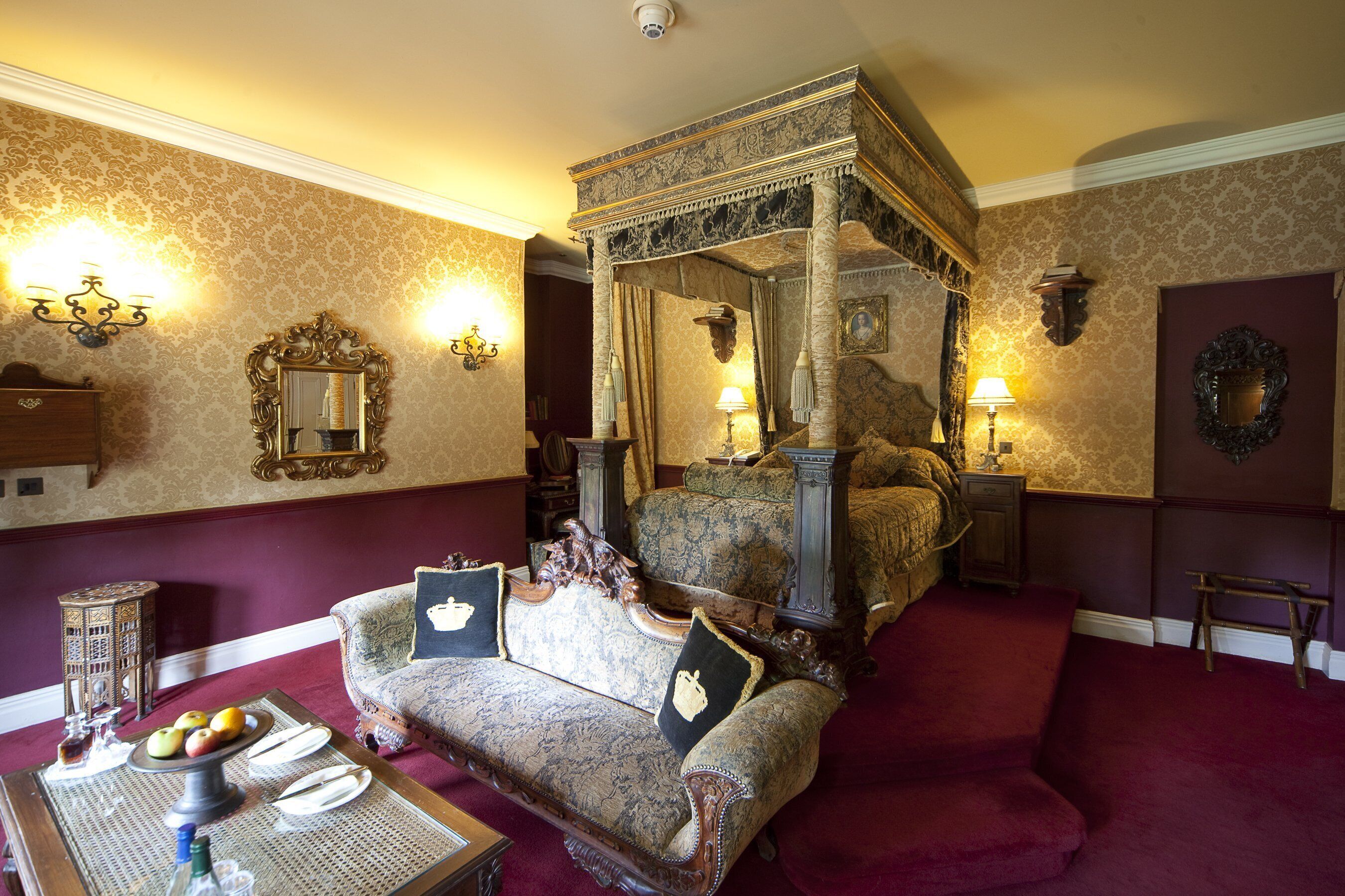 Ein Himmelbett mit aufwendiger Verzierung, ein Vintage-Sofa mit passenden Kissen und ein kleiner Tisch mit Früchten und einer Kerze.