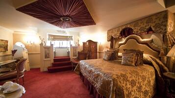A spacious bedroom with a large bed, a desk, and a chair. There is a staircase leading to an upper level.