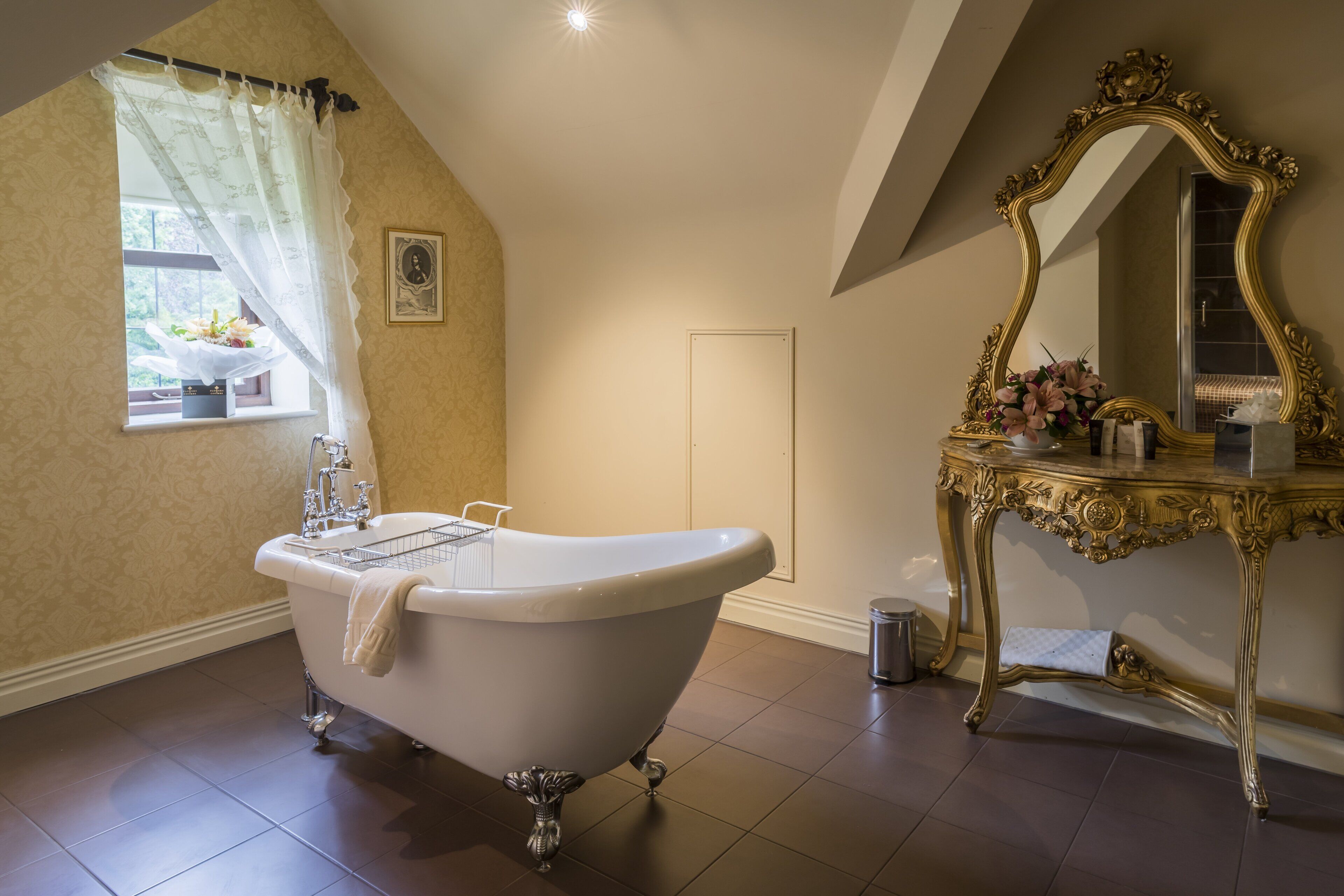 A bathroom with a clawfoot bathtub, a vanity with an ornate mirror, and a window with a curtain.