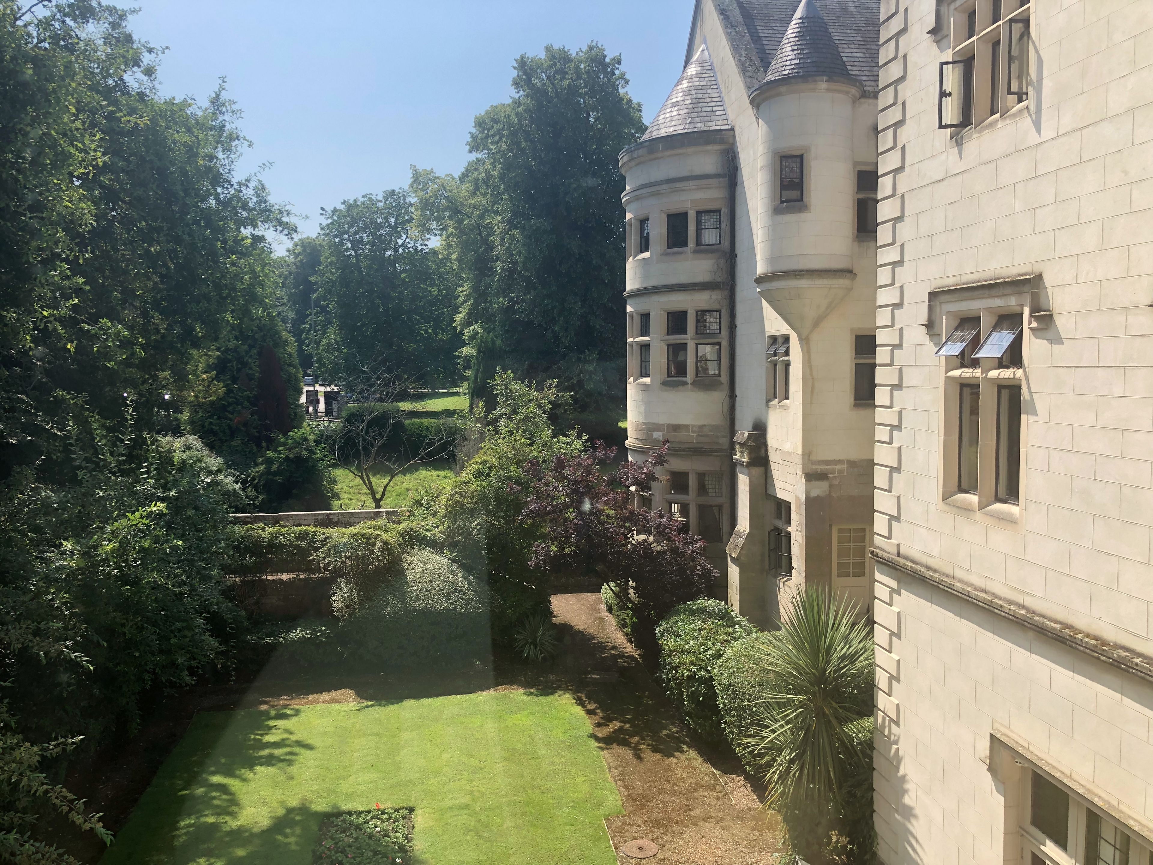 A courtyard with a lawn, a small bridge, and a building with a turret and windows.
