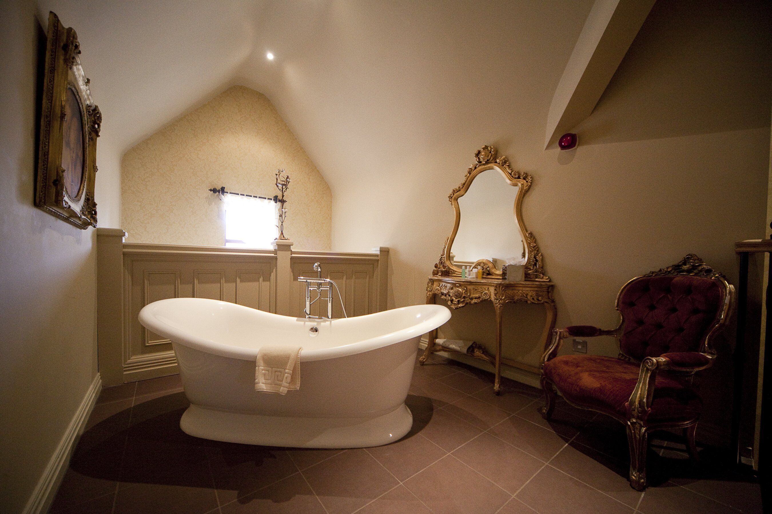 Een badkamer met een vrijstaand bad, een wastafel met spiegel, en een rode fauteuil.