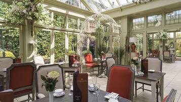 A conservatory with tables and chairs, a glass ceiling, and various plants.