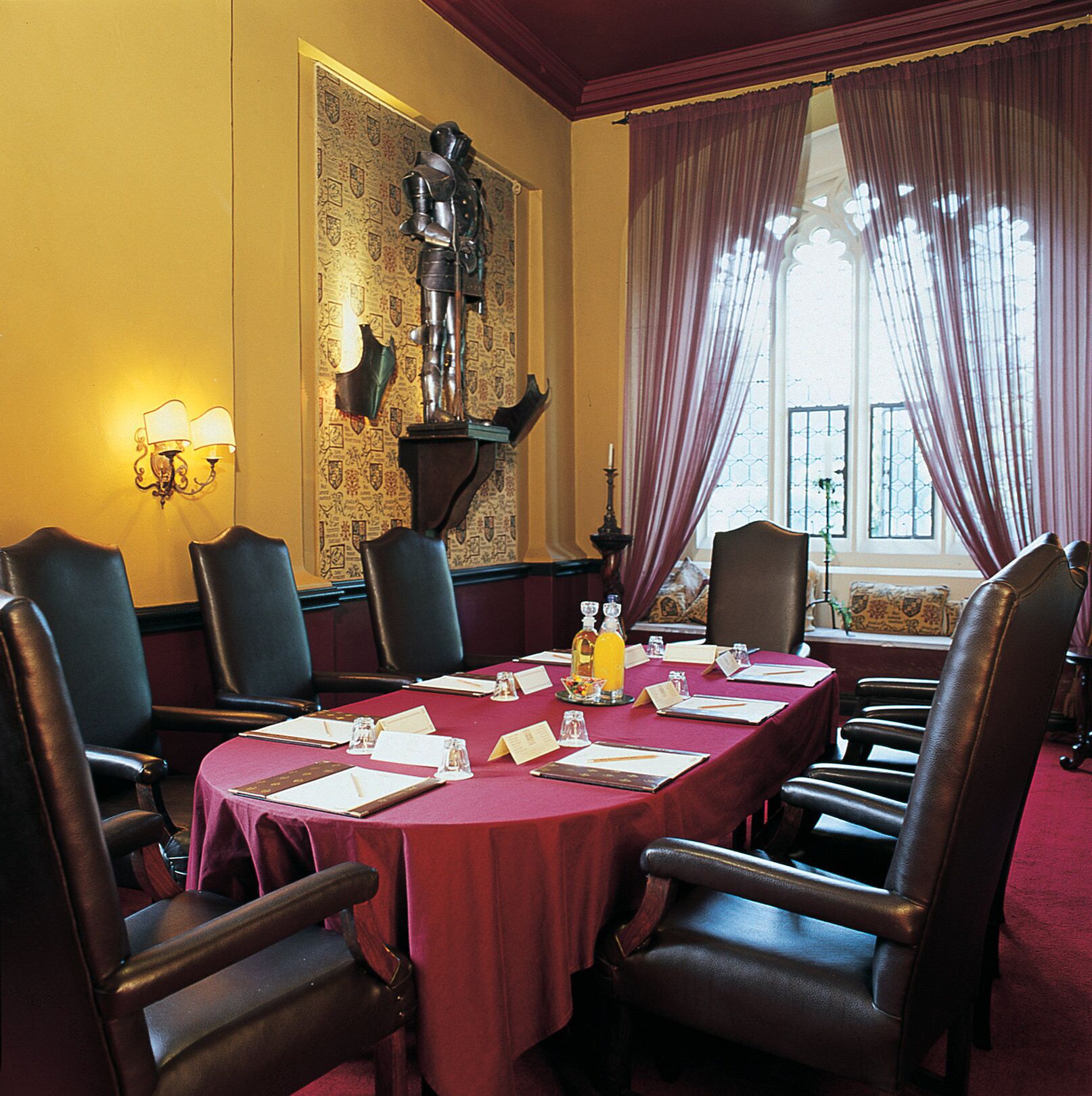 A conference room with a long table, leather chairs, a red tablecloth, and a coat of arms on the wall.