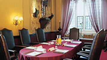 A conference room with a long table, leather chairs, a red tablecloth, and a coat of arms on the wall.