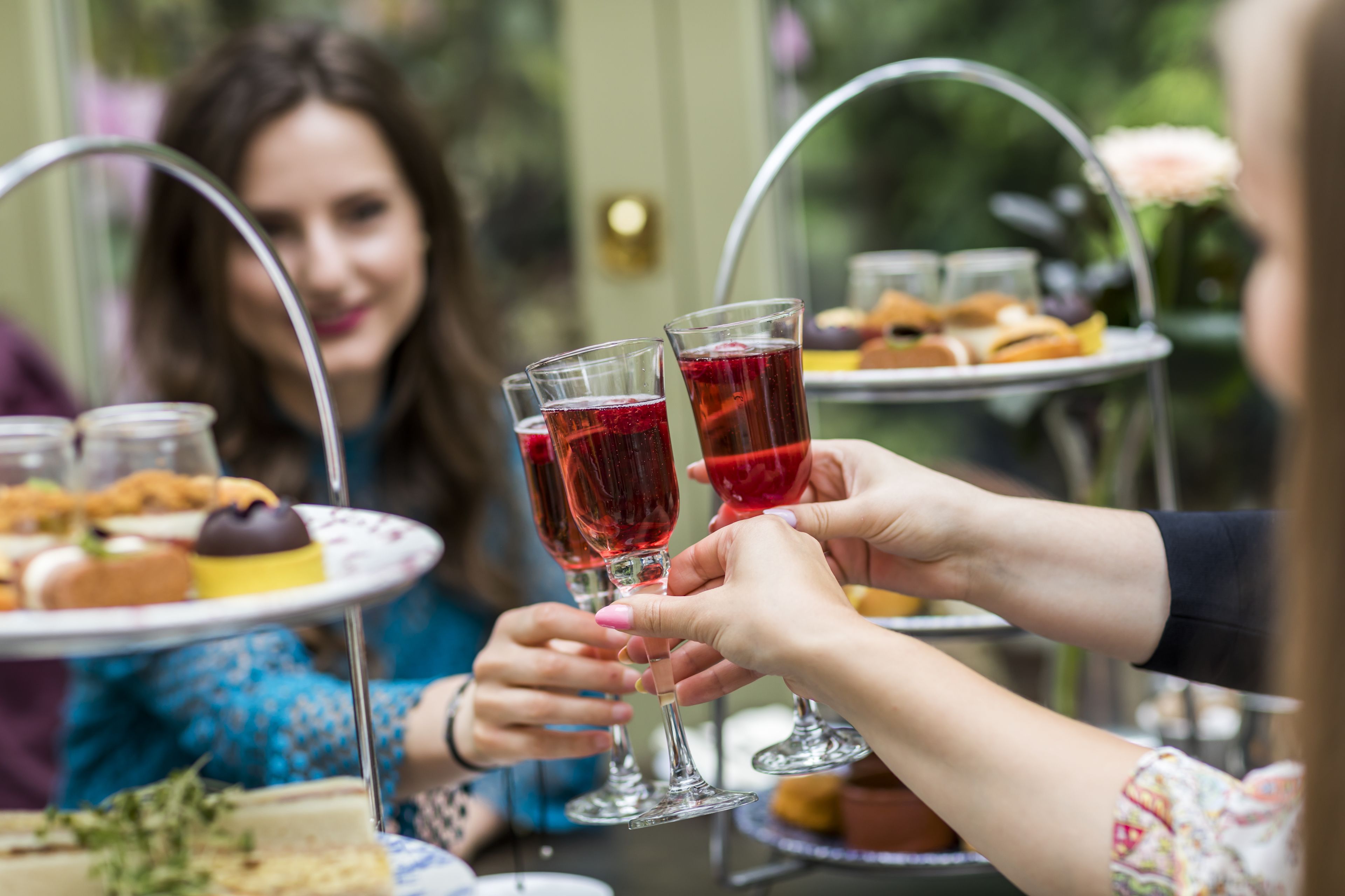 Un groupe de personnes trinquant avec des boissons rouges autour d’une table sur laquelle se trouve un présentoir à gâteaux à plusieurs niveaux.