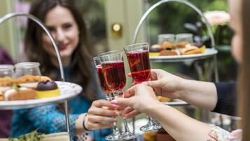 Un grupo de personas brindando con bebidas rojas en una mesa con un pastelero de varios niveles.