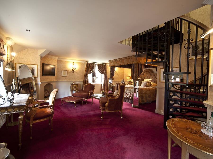 Amplia sala de estar con alfombra roja, muebles elegantes, chimenea y una escalera que conduce a un nivel superior.