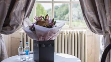 A table with a bouquet of flowers in a box, two bottles, and a radiator in the background.