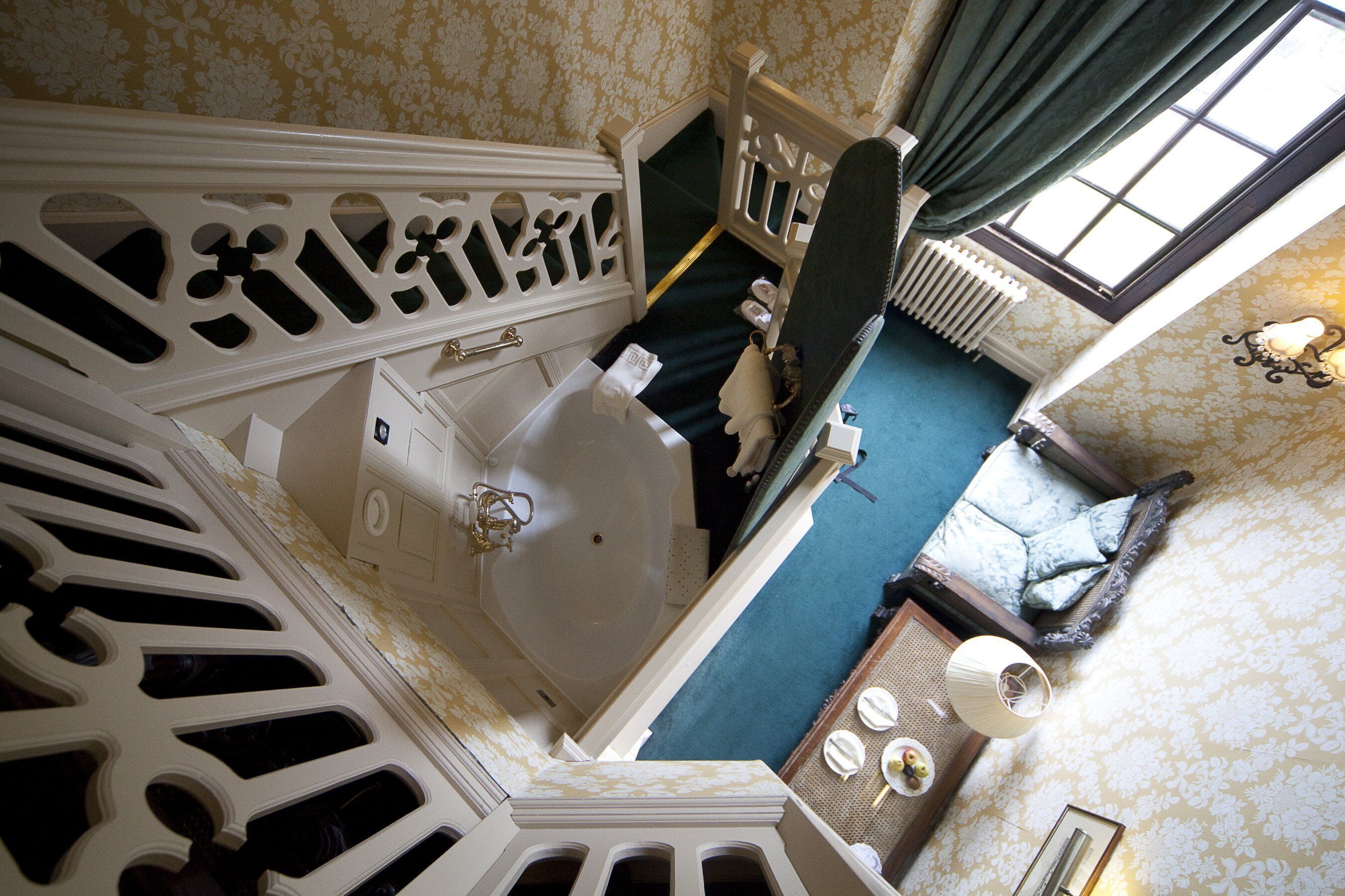 A high-ceilinged room with a large bathtub, a wooden staircase, and a view of the adjacent room.