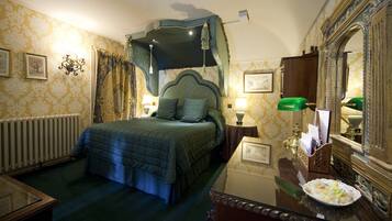 A bedroom with a four-poster bed, a nightstand with a lamp, a dresser, and a mirror.