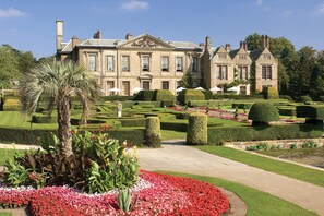 A large, historic building with symmetrical architecture, manicured gardens, and a well-maintained lawn. - Coombe Abbey Hotel (Coventry)